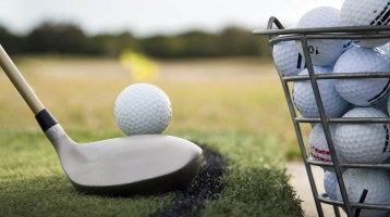 golfer lining up shot next to bucket of golf balls